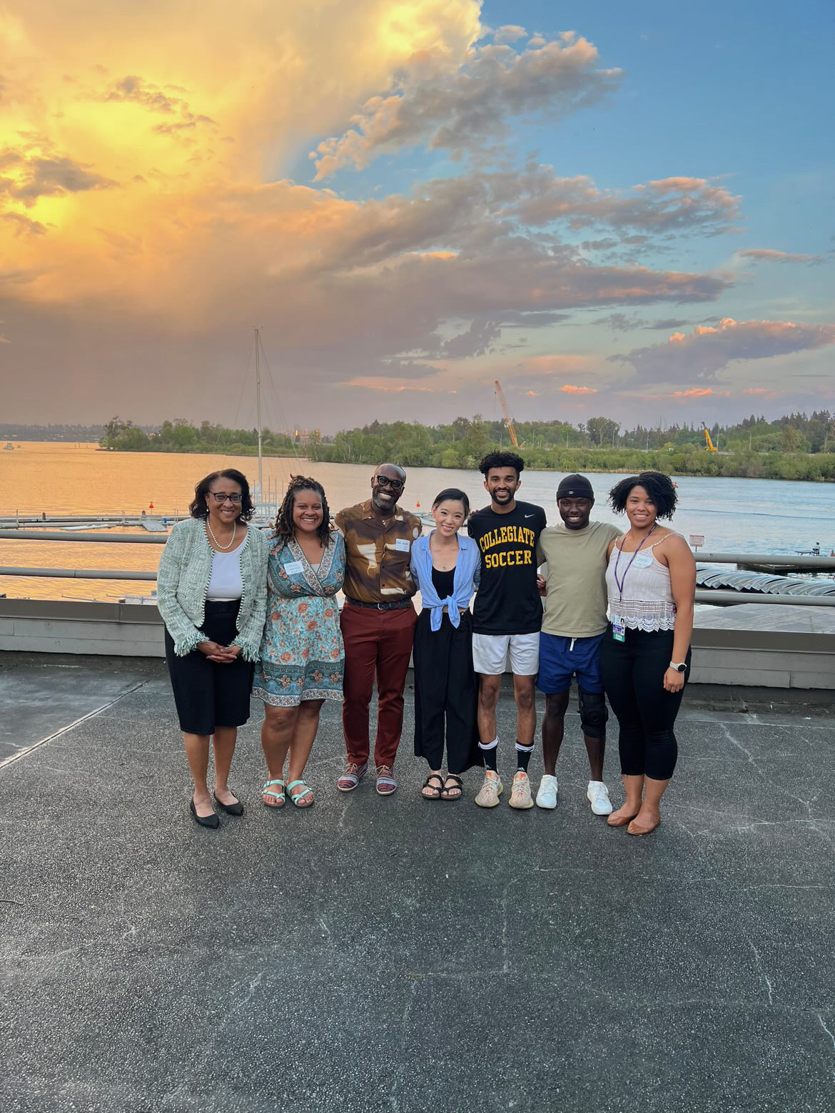 Photo of 6 people posing for a picture  near a lake at sundown.