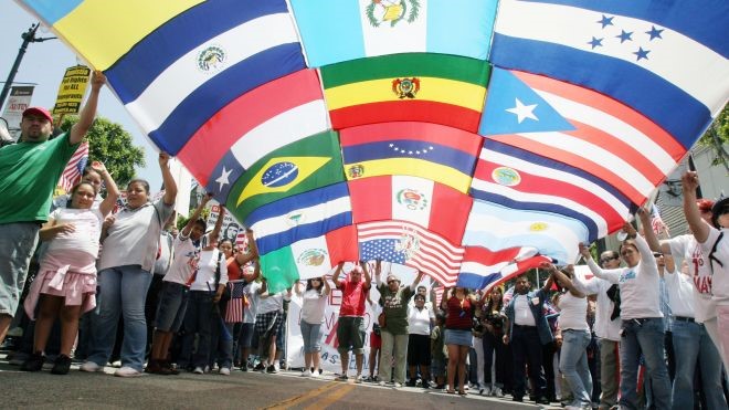 People holding one large flag made up of different Latinx and Hispanic flags
