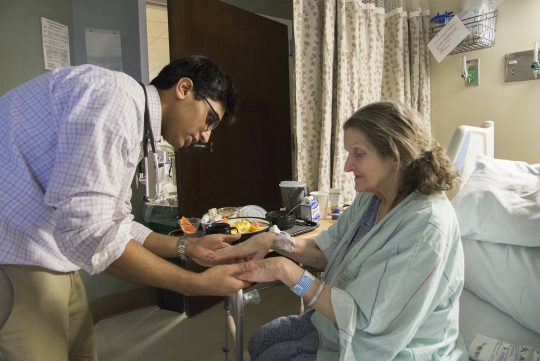 BIPOC student provider examining the hands of a patient in hospital room