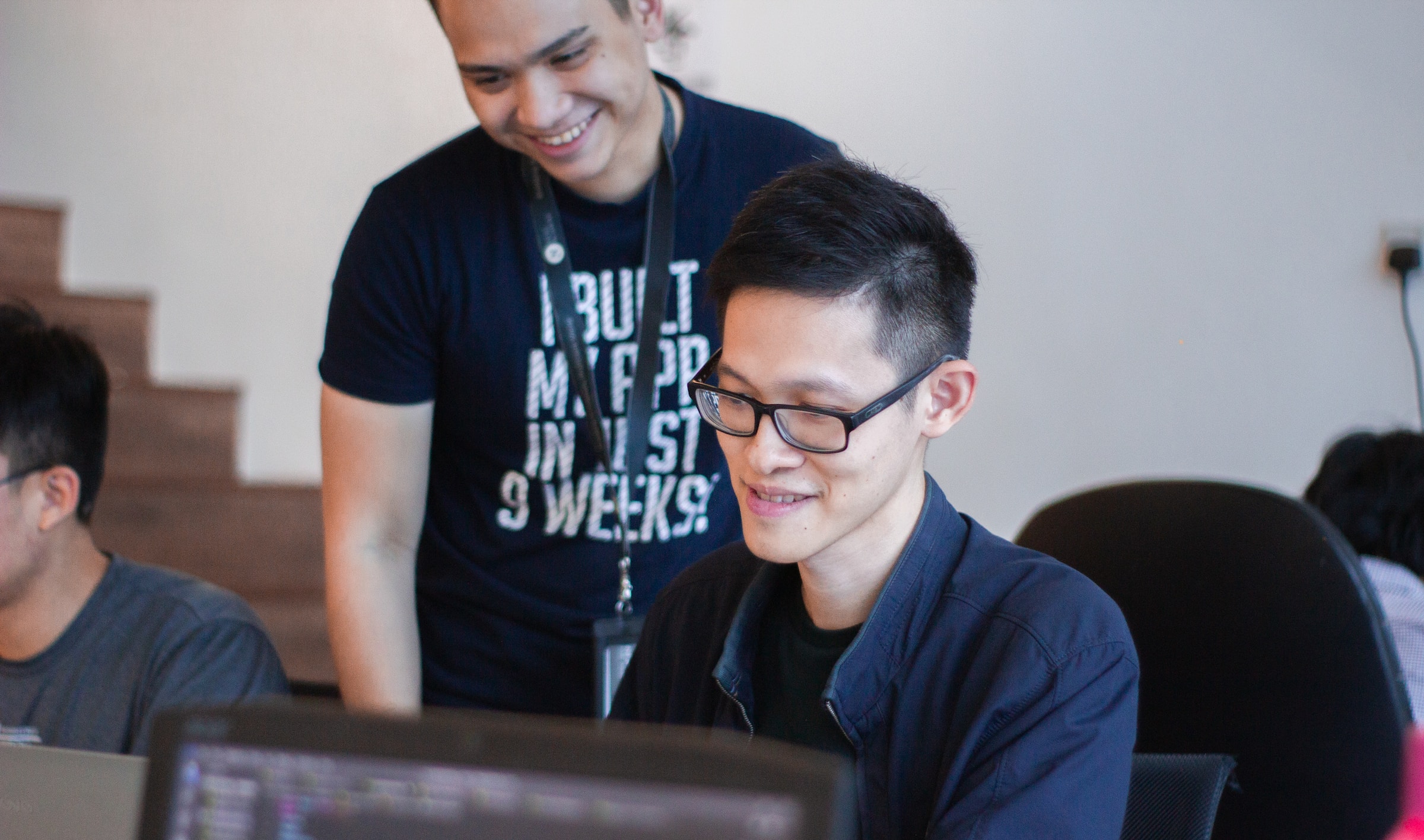 1 person sitting down with a computer and another standing behind.