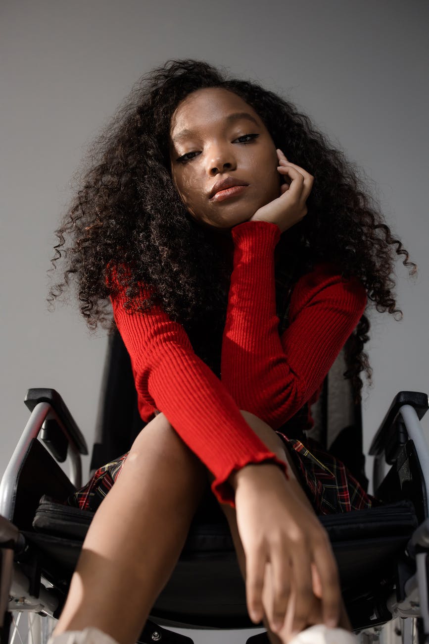 a woman in red knitted sweater sitting on wheelchair with her hand on her chin