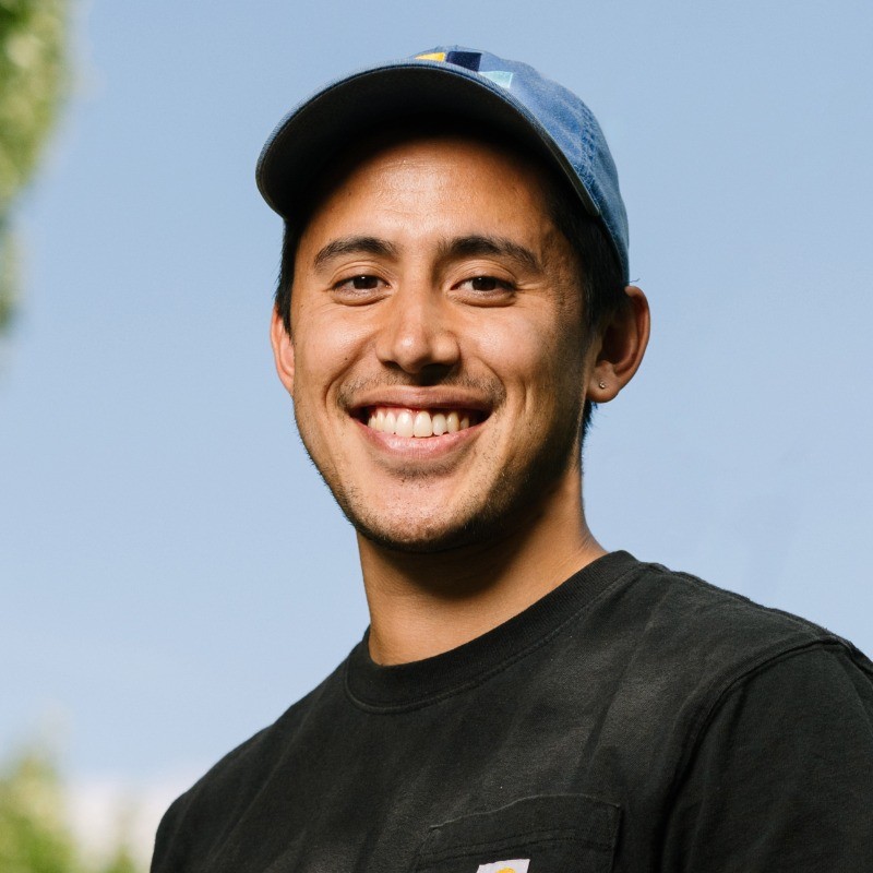 Photo headshot of Quin Nelson smiling individual, wearing a blue hat and black shirt.