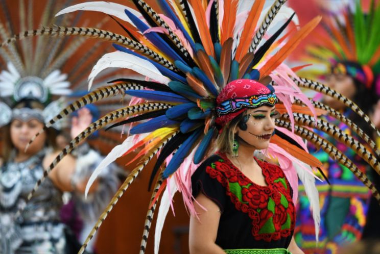 Photo of someone dressed in Dia de los Muertos clothing with a large feathered headdress.